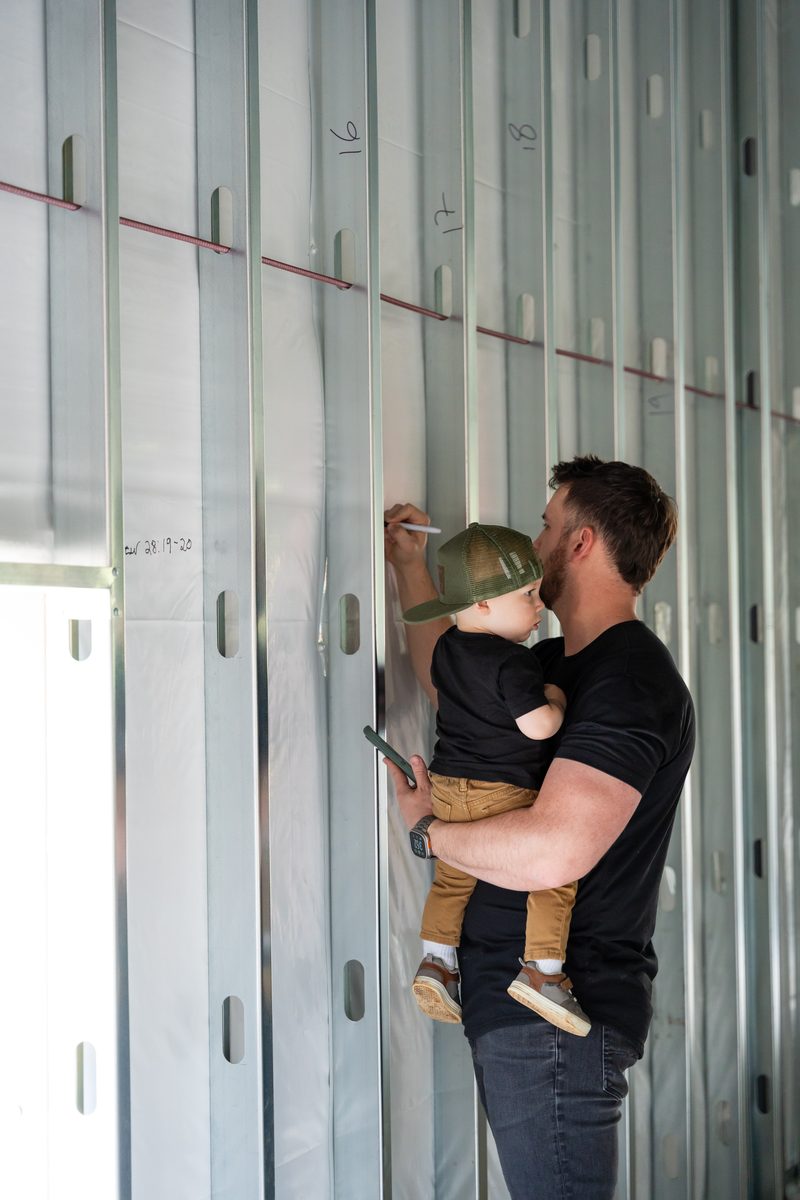 Father holding a child while writing on construction framing